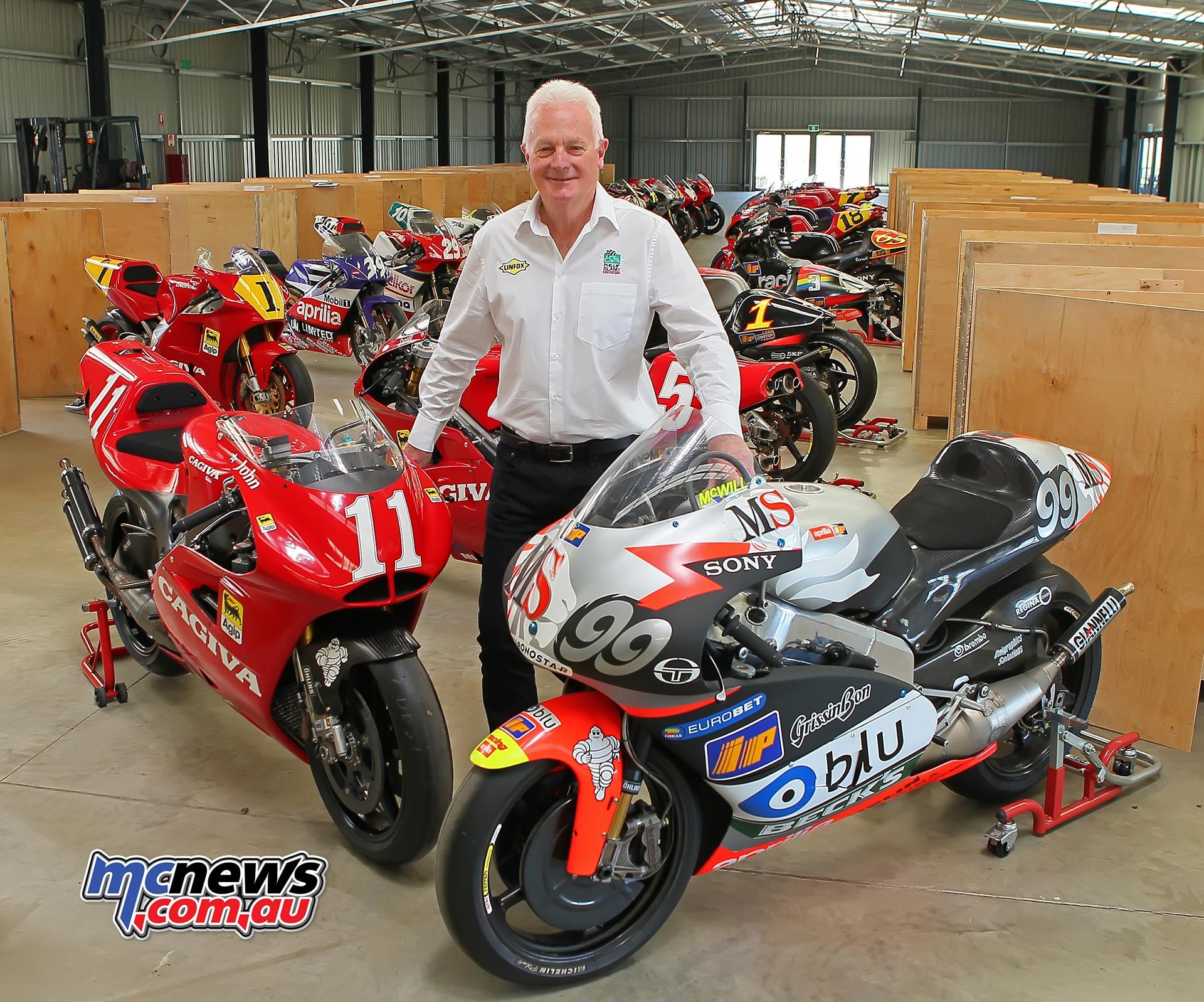 Fergus Cameron standing among historic racing motorcycles and wooden packing cases at Phillip Island.