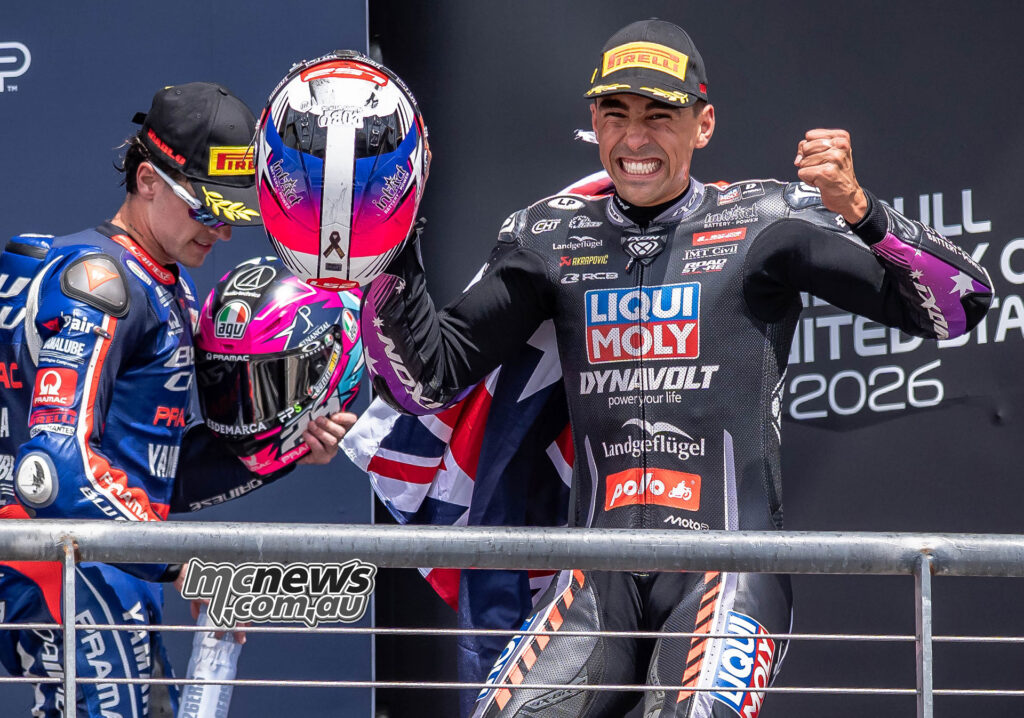 Senna Agius celebrates on the Moto2 podium at COTA with an Australian flag behind him.