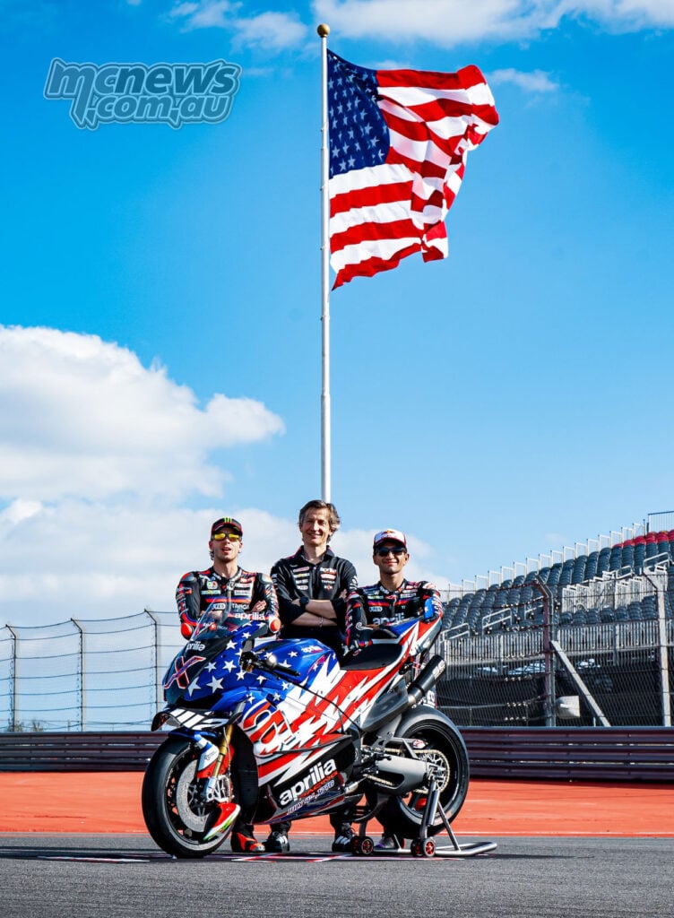 Aprilia Racing team members pose with the Aprilia X 250TH under a large American flag at COTA.