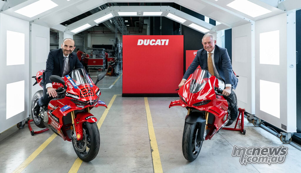Two officials sit on Ducati motorcycles inside a bright display tunnel at Borgo Panigale.