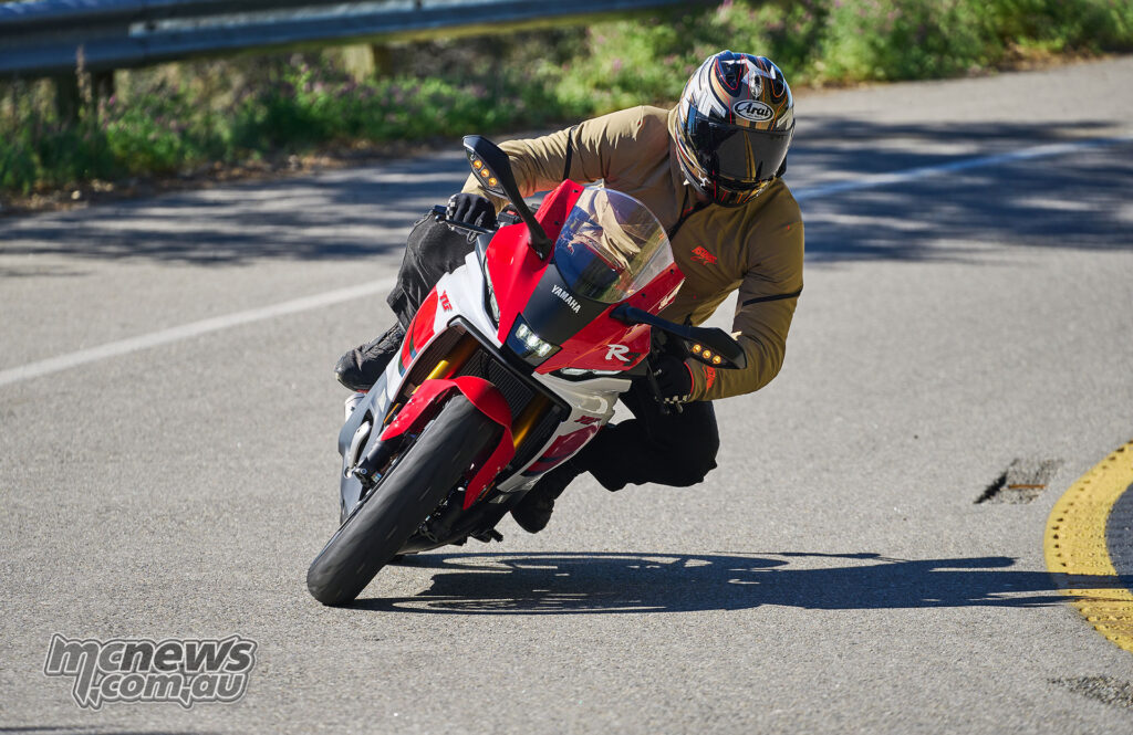 Rider cornering red 2026 Yamaha YZF-R7 toward camera on public road.