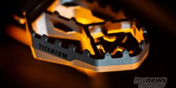 Close-up of Akrapovič titanium adventure footpeg showing serrated teeth and machined platform.