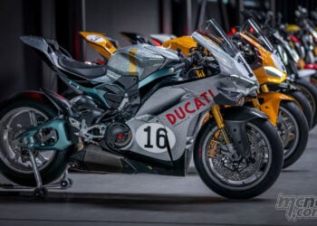 Studio lineup of Ducati Collection 100 motorcycles, led by a silver Panigale V4 S 100, with multiple anniversary models arranged behind it.
