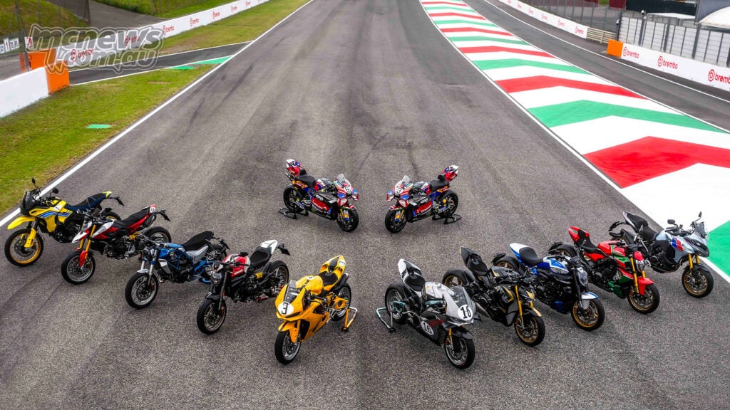 Overhead view of Ducati Collection 100 motorcycles arranged on a circuit surface with two Ducati MotoGP bikes positioned in the centre.