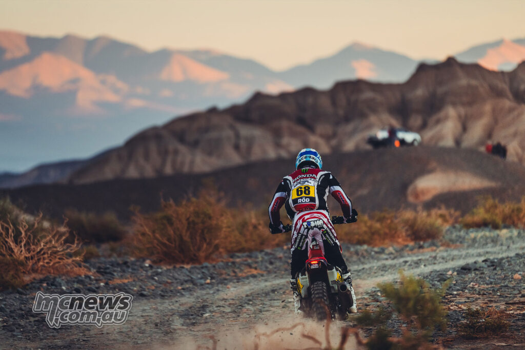 Tosha Schareina rides a Honda rally bike away from the camera on a rocky desert track.
