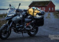 Ducati Multistrada V4 packed with touring luggage on a coastal road near a red building in northern Europe.