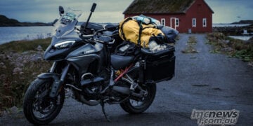 Ducati Multistrada V4 packed with touring luggage on a coastal road near a red building in northern Europe.