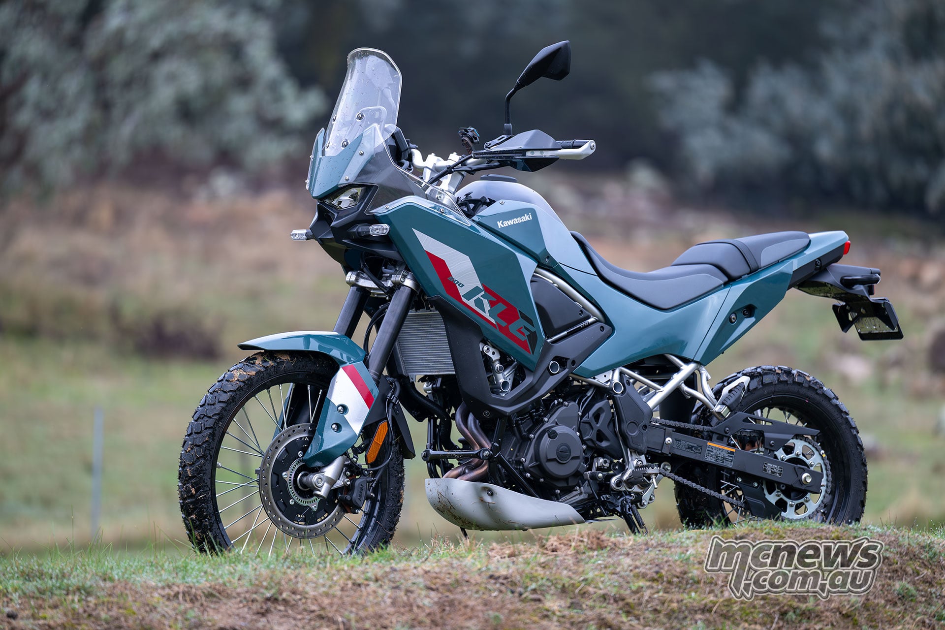 Blue-green Kawasaki KLE500 SE parked on grass, viewed from the front left with its windscreen, handguards and skid plate visible.
