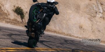 Landscape image of the 2026 Kawasaki Z1100 SE ABS carrying a high wheelie on a twisty road.