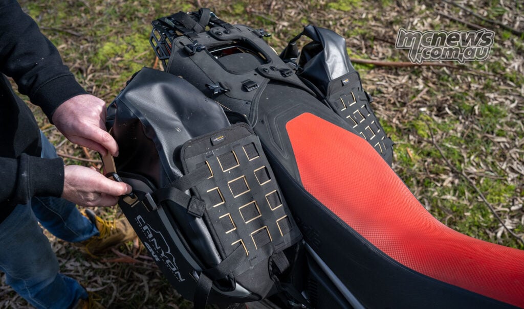 Close-up of the lower Givi Canyon mounting straps and soft bag positioned beside the Aprilia Tuareg 660 exhaust.
