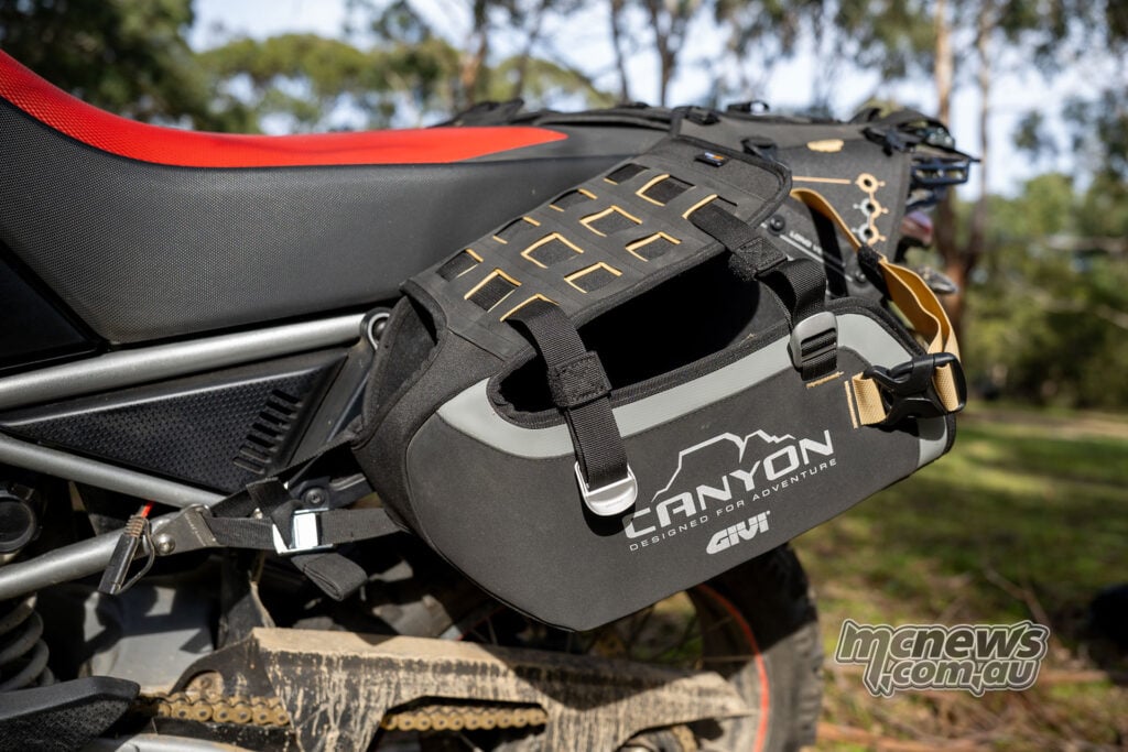 Rider carrying a removable black Givi Canyon motorcycle side bag by its handle.