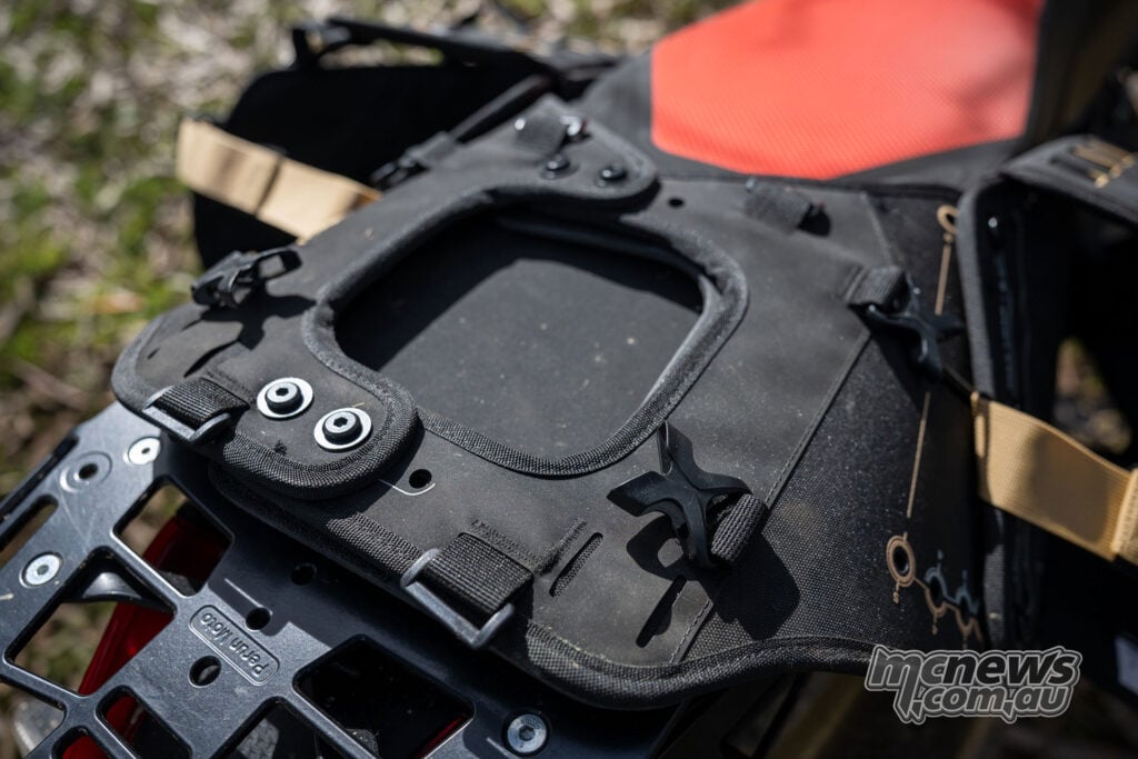 Hands fastening a quick-release buckle on a Givi Canyon side bag fitted to an Aprilia Tuareg 660.