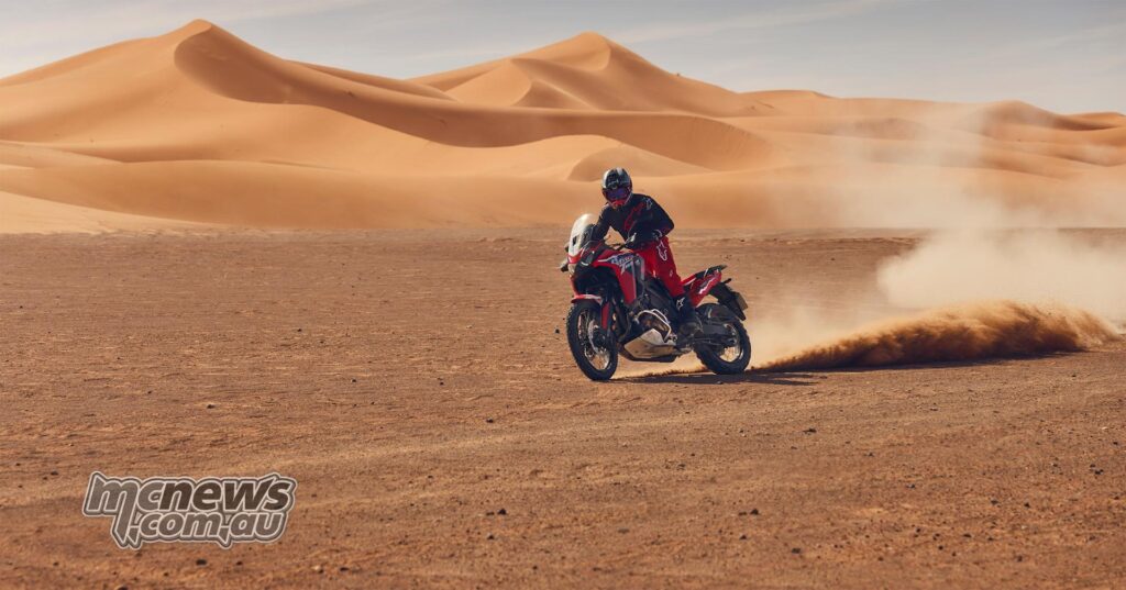 The rider is sliding the red 2026 Honda Africa Twin ES DCT across a sandy desert landscape.