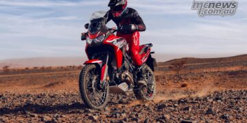 Rider standing on a red 2026 Honda Africa Twin while crossing rocky desert terrain.