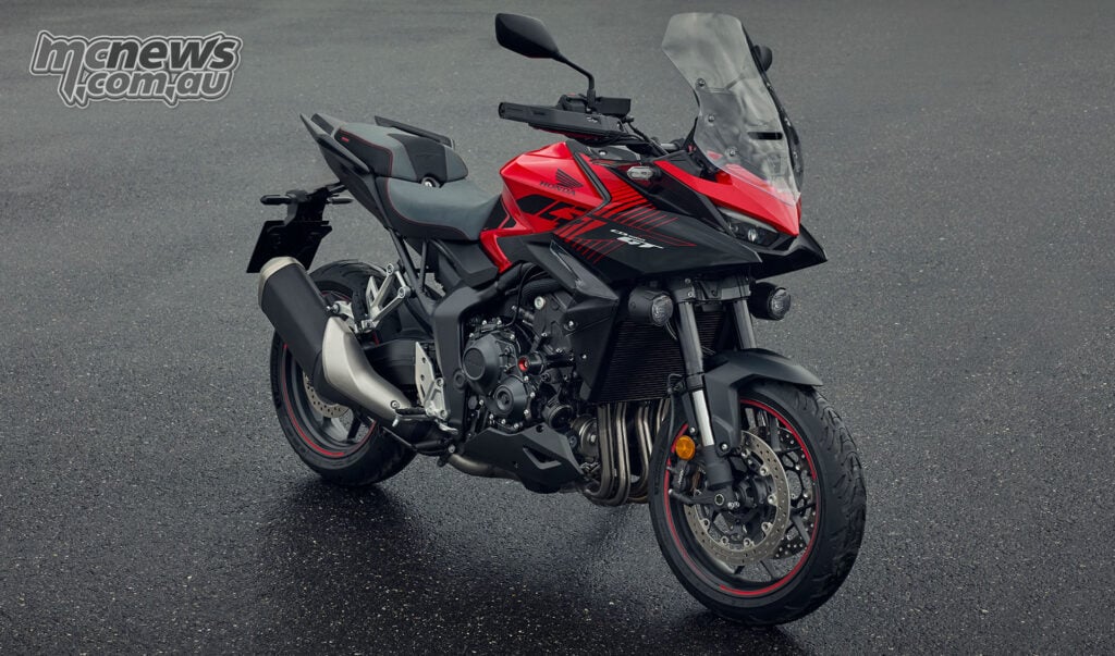 Front three-quarter view of a red 2026 Honda CB1000GT with hand guards, windscreen and auxiliary lights.