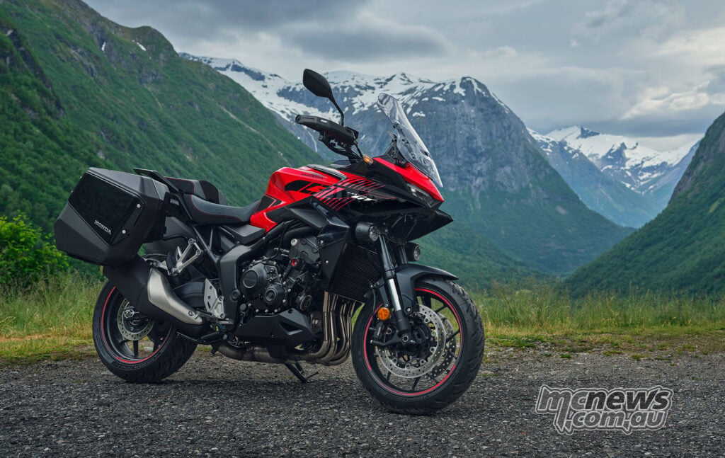 Red 2026 Honda CB1000GT parked in a mountain valley with panniers, tall windscreen and auxiliary lights.