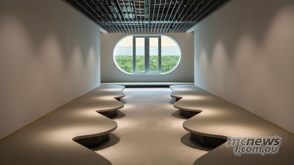 Modern Moto Guzzi interior featuring sculpted gray benches, a slatted roof and a large circular window.