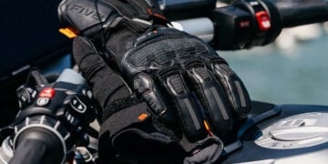 Pair of black FIVE GT1 EVO GTX motorcycle touring gloves resting on a motorcycle at a petrol station.
