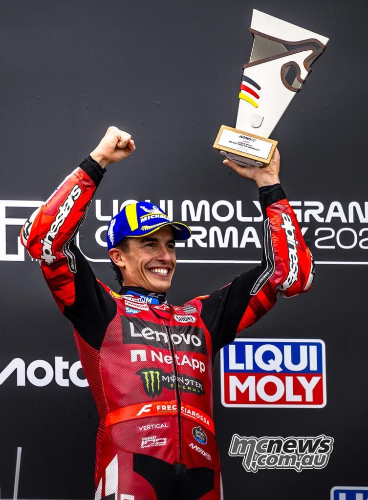 Marc Marquez holds the 2026 German MotoGP winner’s trophy above his head on the Sachsenring podium.