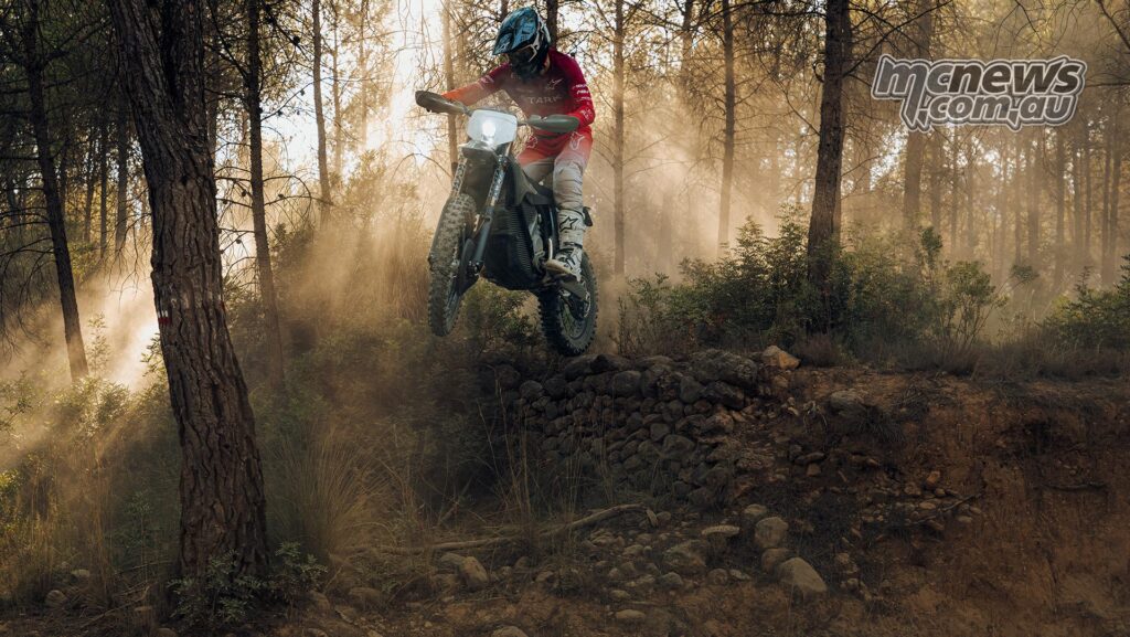 Ryder jumping on the Stark VARG EX Factory Edition through a sunlit forest.