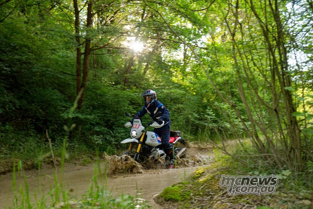 Rider charges the BMW R 12 G/S GS Trophy Competition Bike through a muddy forest water crossing.