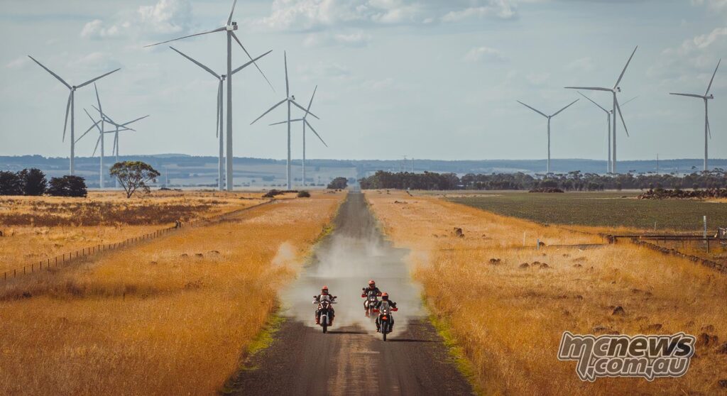 KTM adventure motorcycles ride down a straight gravel road through a Victorian wind farm.
