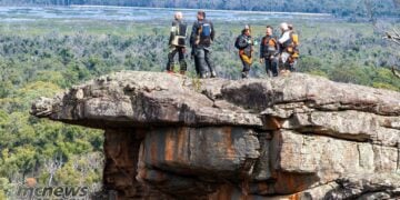 KTM Adventure Rallye riders standing on a rocky lookout above the Grampians landscape.