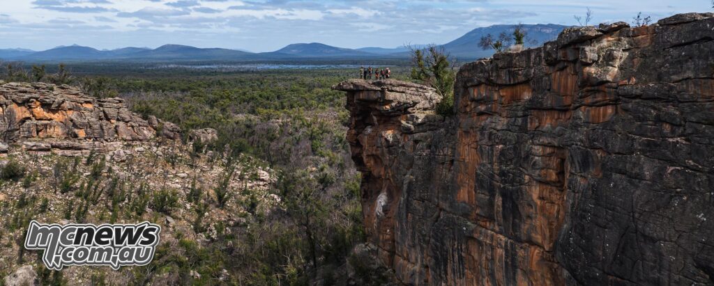 KTM Adventure Rally riders stand on a high sandstone cliff overlooking the Grampians.