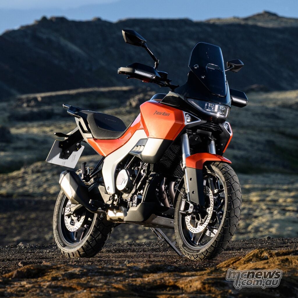 Orange Norton Atlas Apex parked on rocky Icelandic terrain, viewed from the front right.