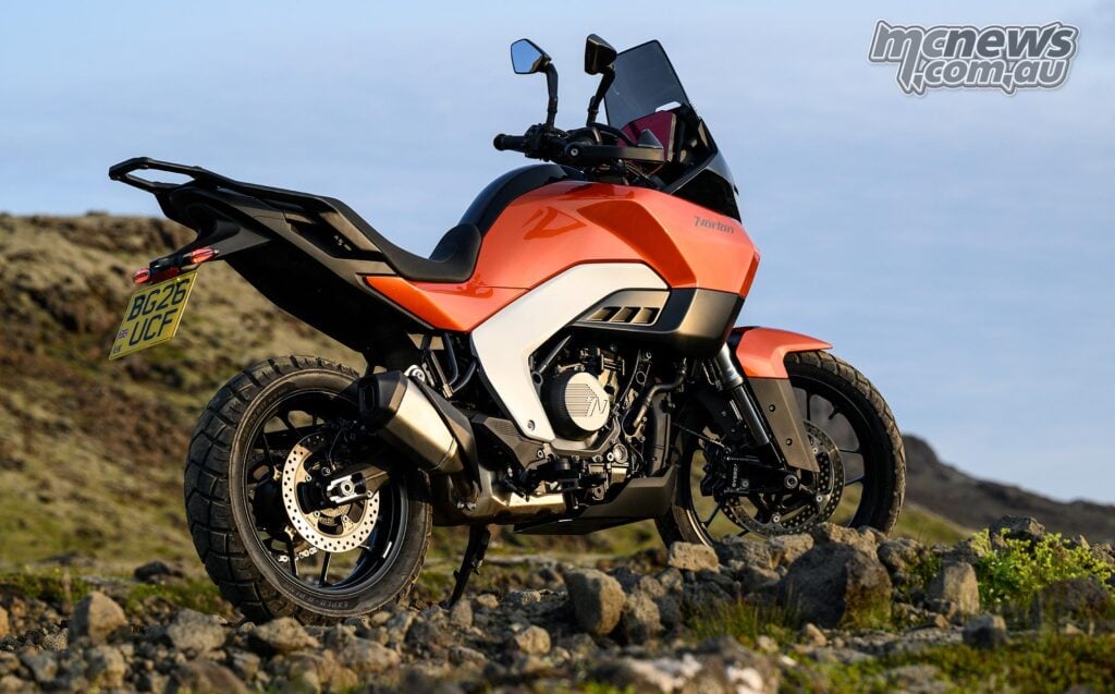 Orange Norton Atlas Apex parked on rocky ground, viewed closely from the rear right