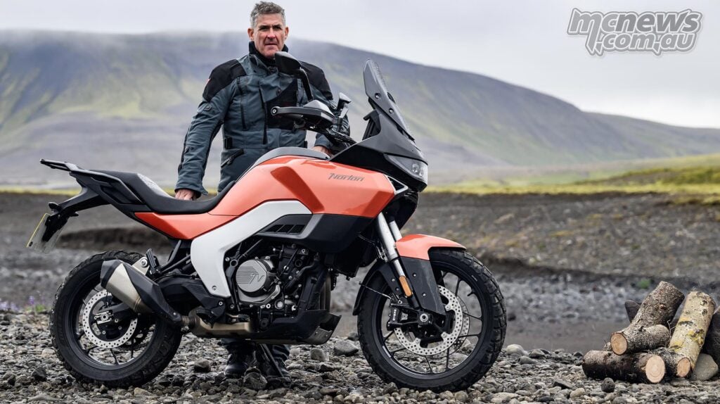 Rider standing beside an orange Norton Atlas on rocky Icelandic ground.