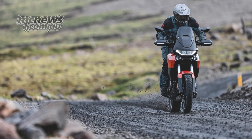 Rider aboard an orange Norton Atlas on a wet Icelandic road.