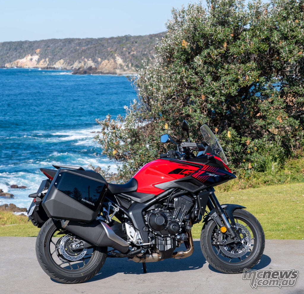 Red 2026 Honda CB1000GT with integrated panniers parked at a coastal lookout.
