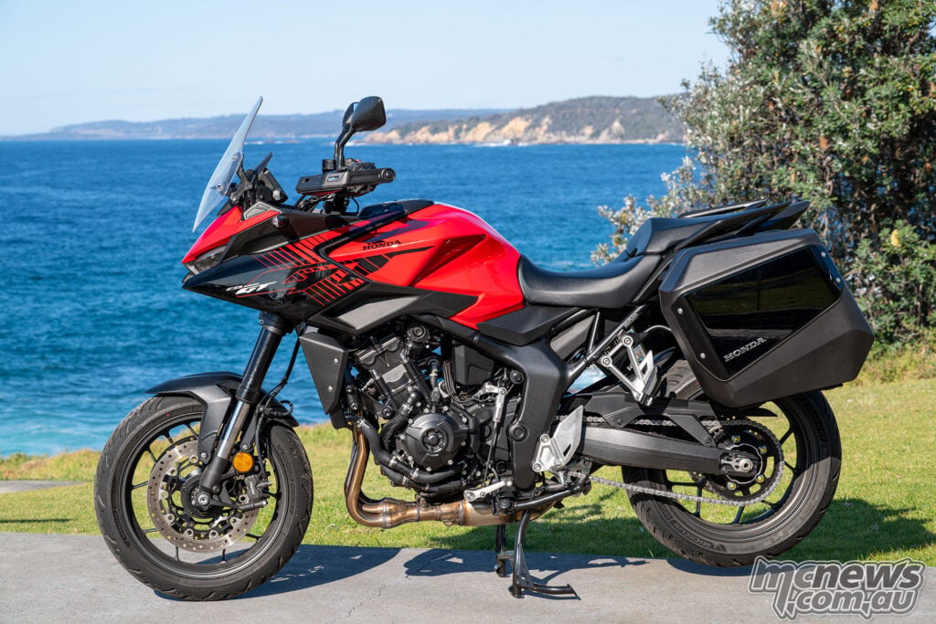 Left-side profile of a red Honda CB1000GT with panniers at a coastal lookout.