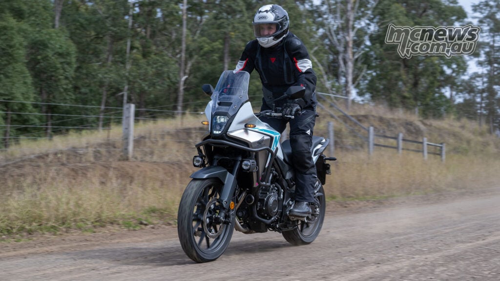Trevor Hedge standing on the footpegs of a Honda NX500 on a gravel road