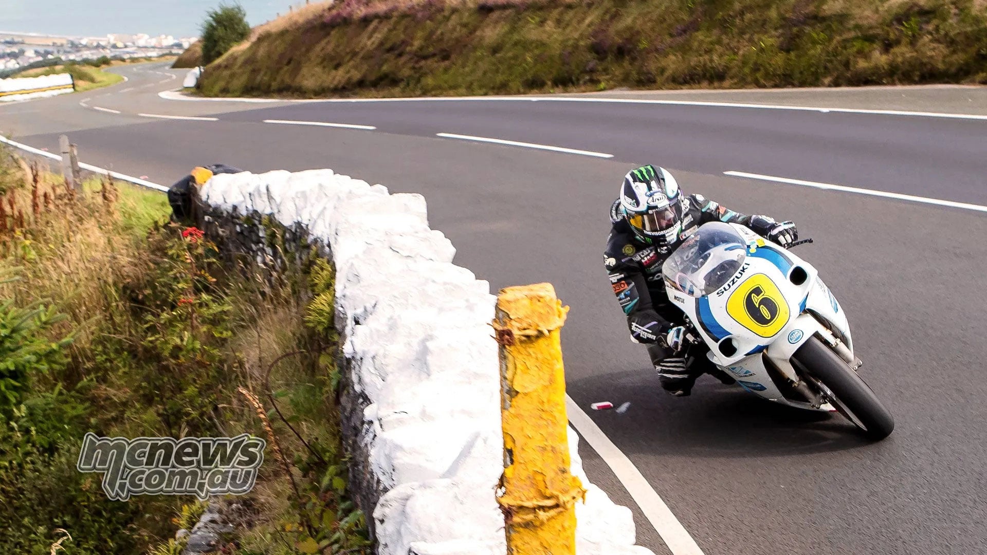Michael Dunlop leans his number six Suzuki through a bend beside a white stone wall