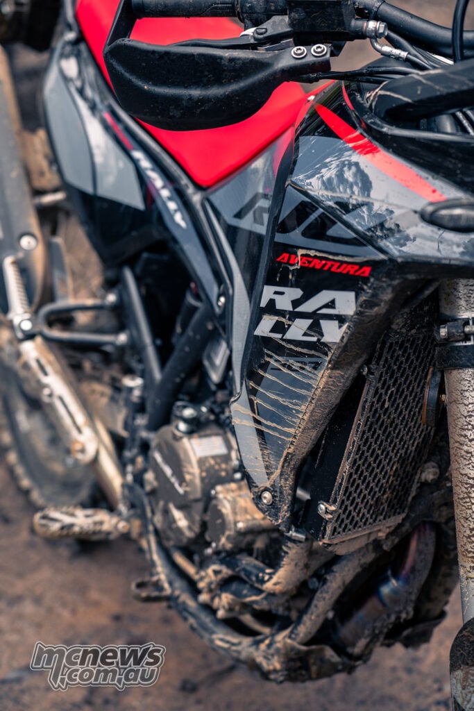 Close-up of the mud-splattered Rieju Aventura Rally 307 side fairing, red seat and handguard