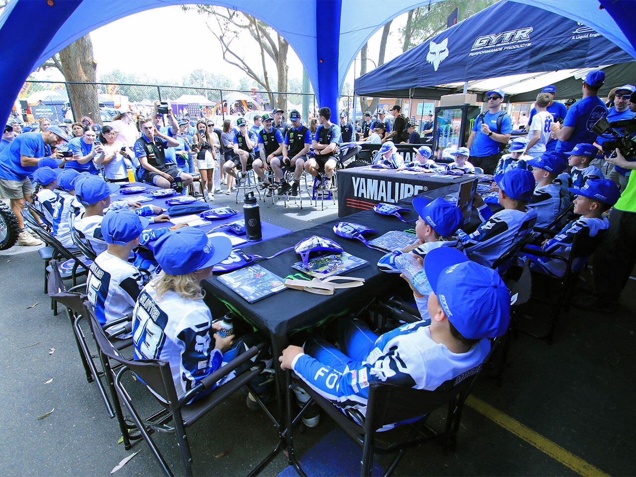 Young Yamaha YZ65 Cup riders seated together beneath a Yamaha paddock awning