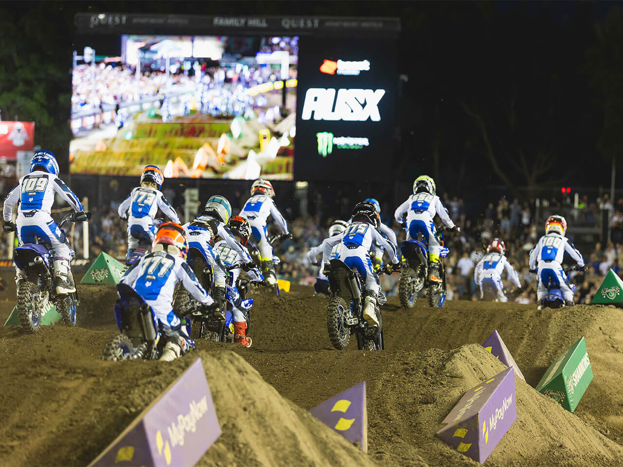 Yamaha YZ65 Cup riders heading onto an indoor Supercross track beneath a large video screen