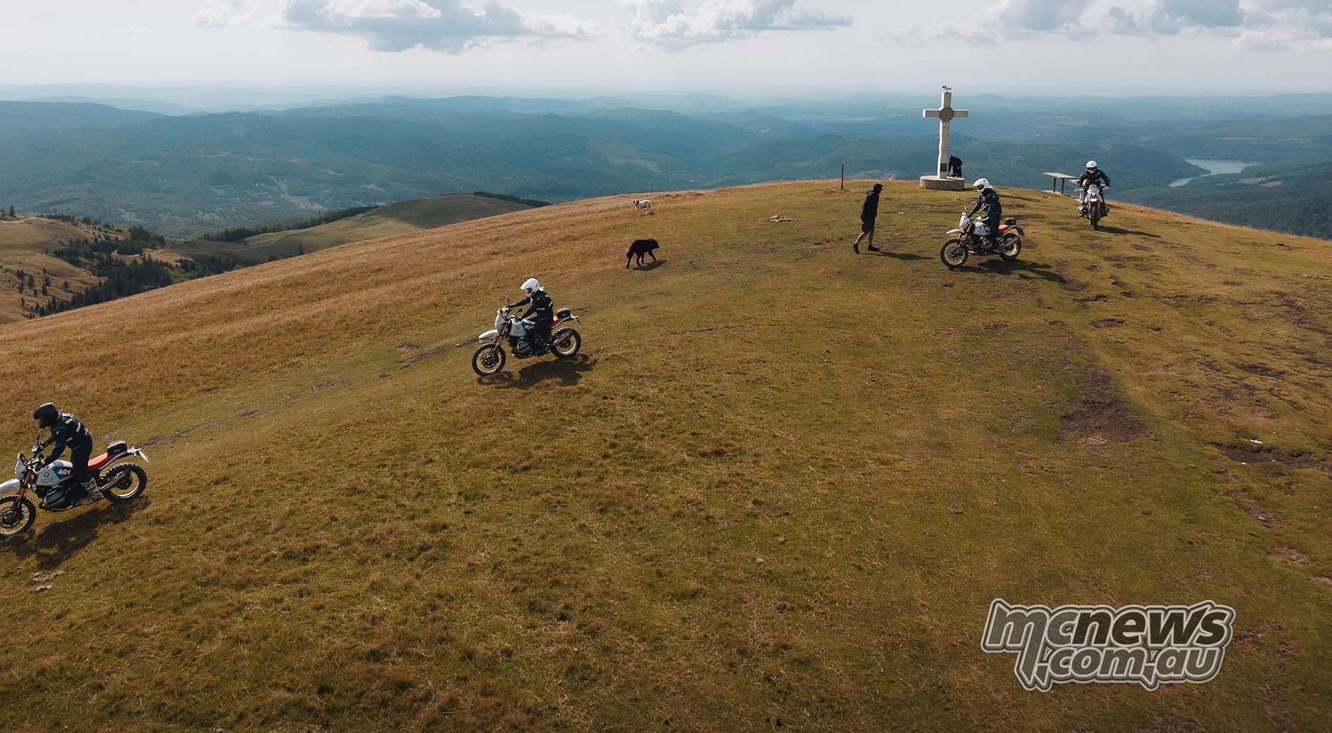 BMW GS Trophy riders cross an open grassy mountain ridge in Romania beneath low cloud.
