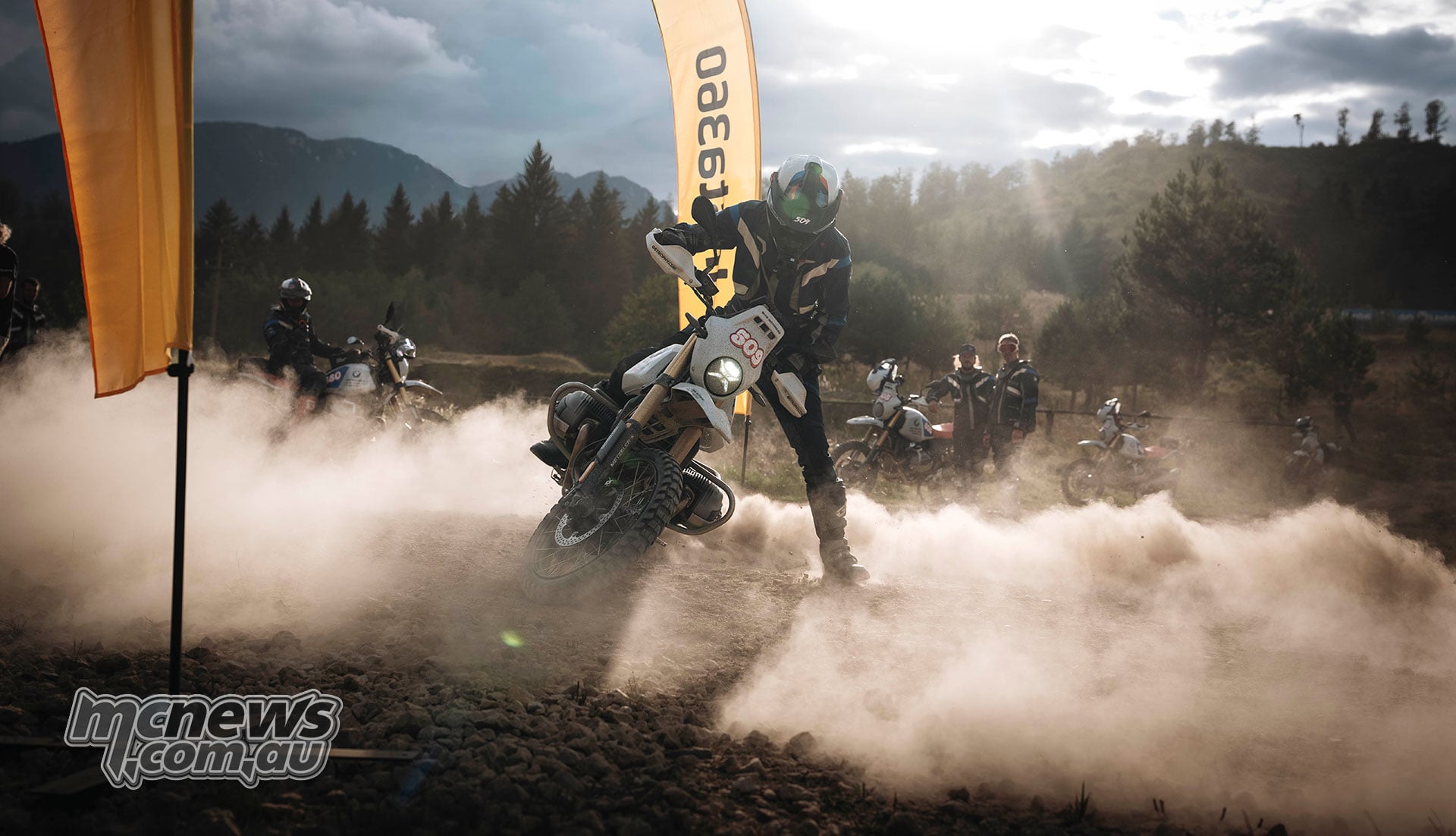 A BMW R 12 G/S rider leans through a loose gravel turn beside GS Trophy course banners, raising a cloud of dust.
