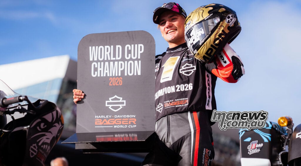 Archie McDonald holds a World Cup Champion 2026 board and raises his gold Kabuto helmet beside the race bikes.