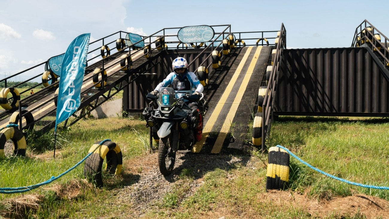 An MT Challenge rider descends a steep metal ramp between tyre barriers.