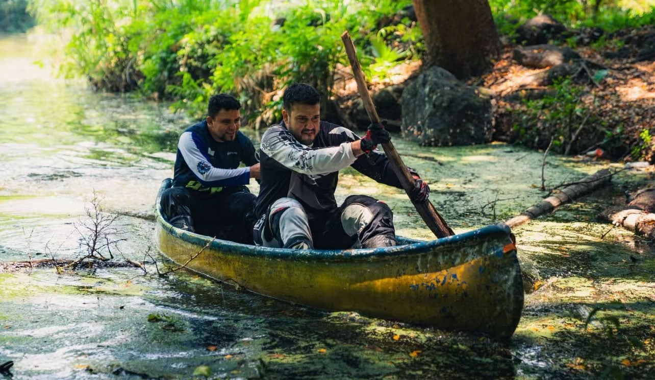 Two MT Challenge participants paddle a small boat through a shaded waterway.