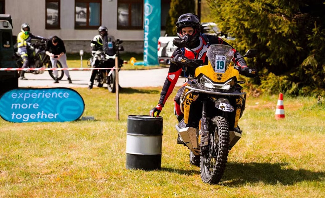 Rider number 19 reaches towards a ball on a drum while balancing an adventure motorcycle.