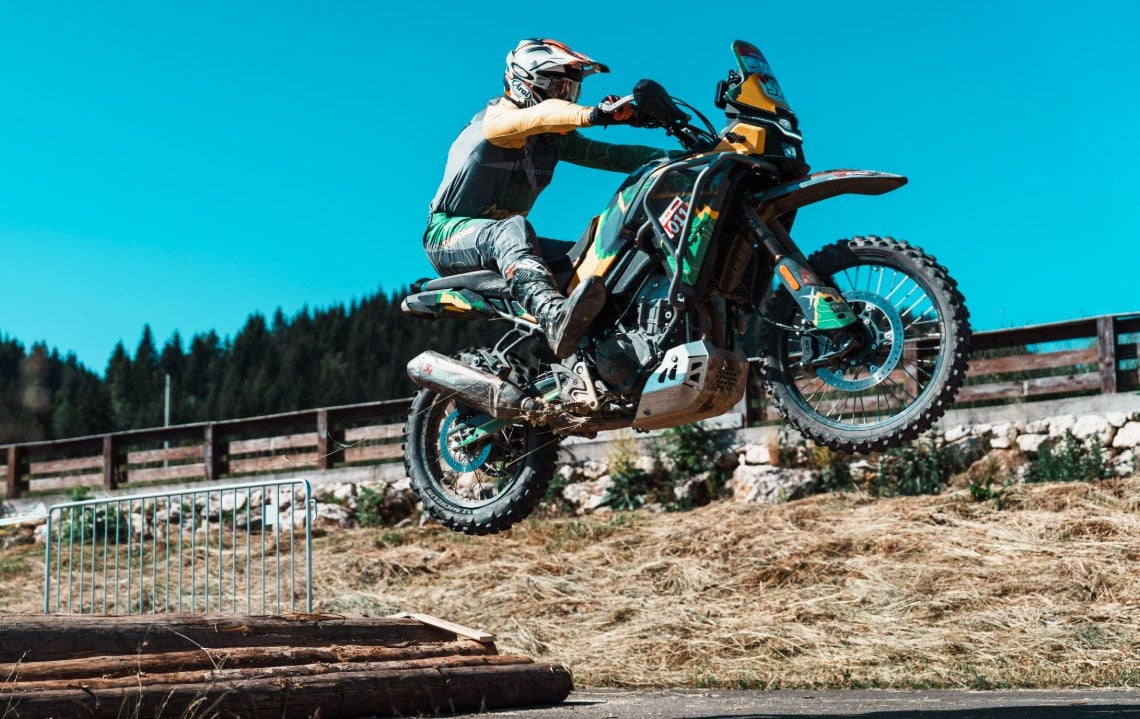 An adventure motorcycle rider jumps over a log obstacle during an MT Challenge event.