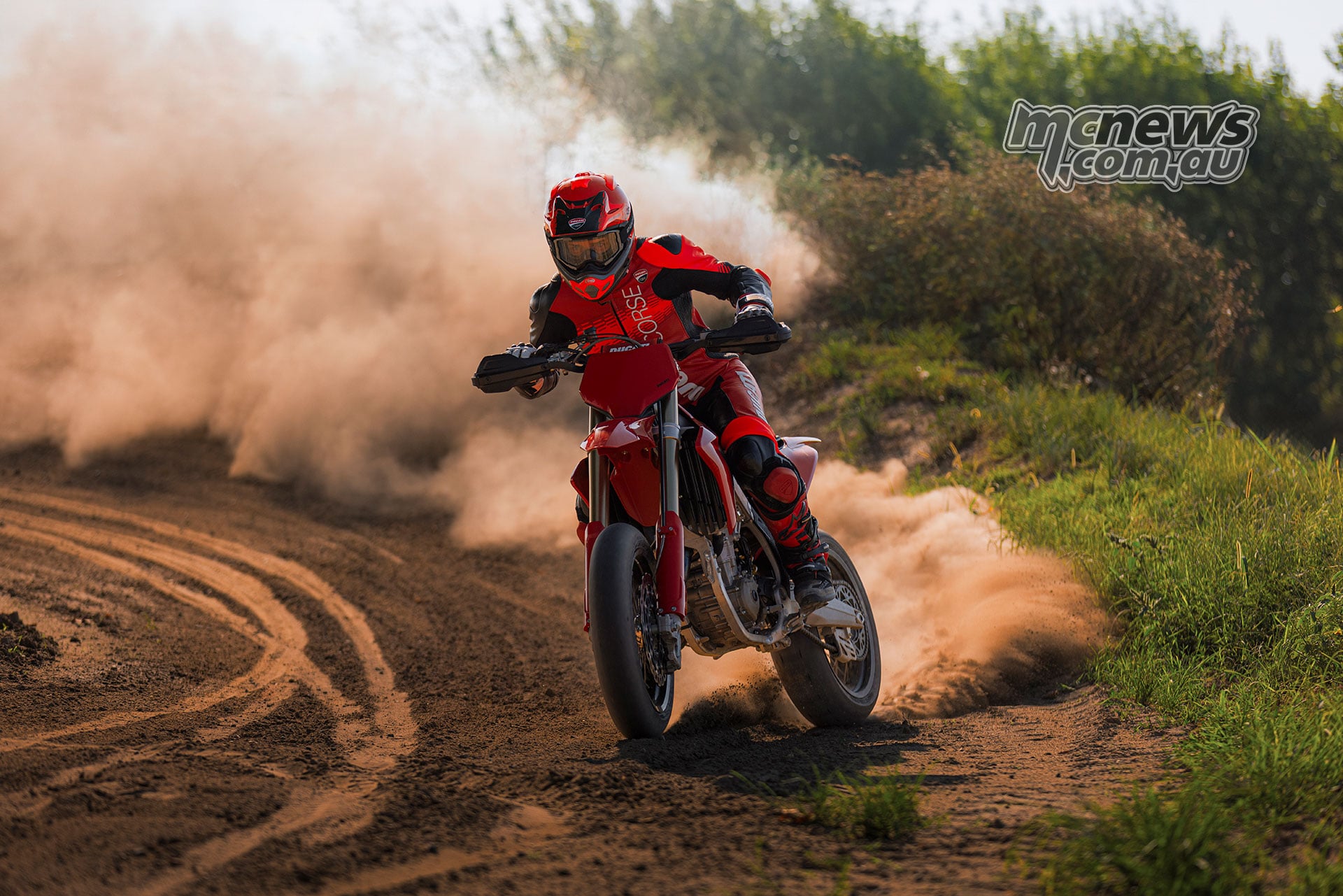Rider approaches on the Ducati Desmo450 SM through a dirt section, trailing a cloud of dust behind the motorcycle.