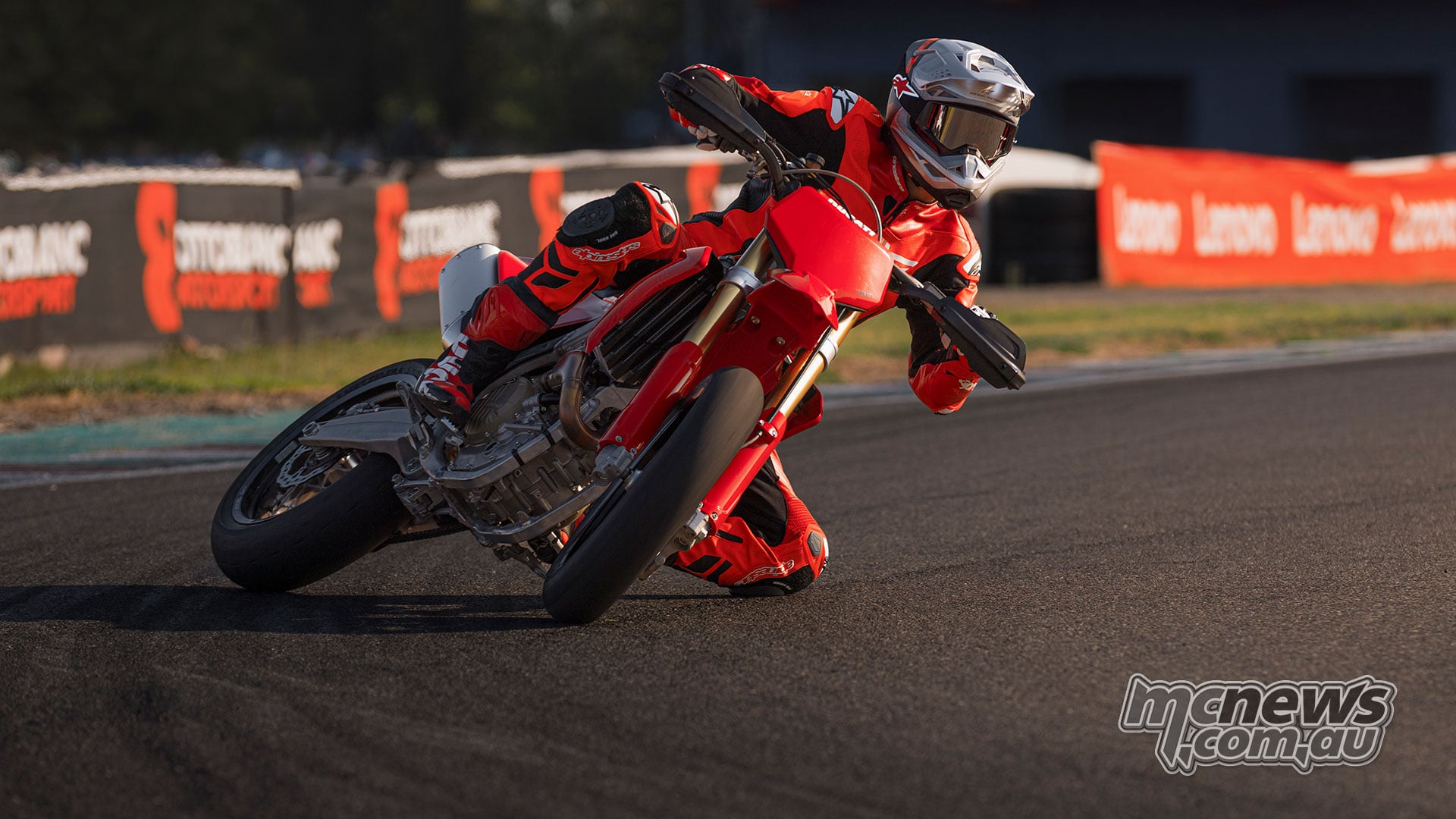 Rider in red leathers leans the Ducati Desmo450 SM into a tarmac corner with a knee extended towards the track.