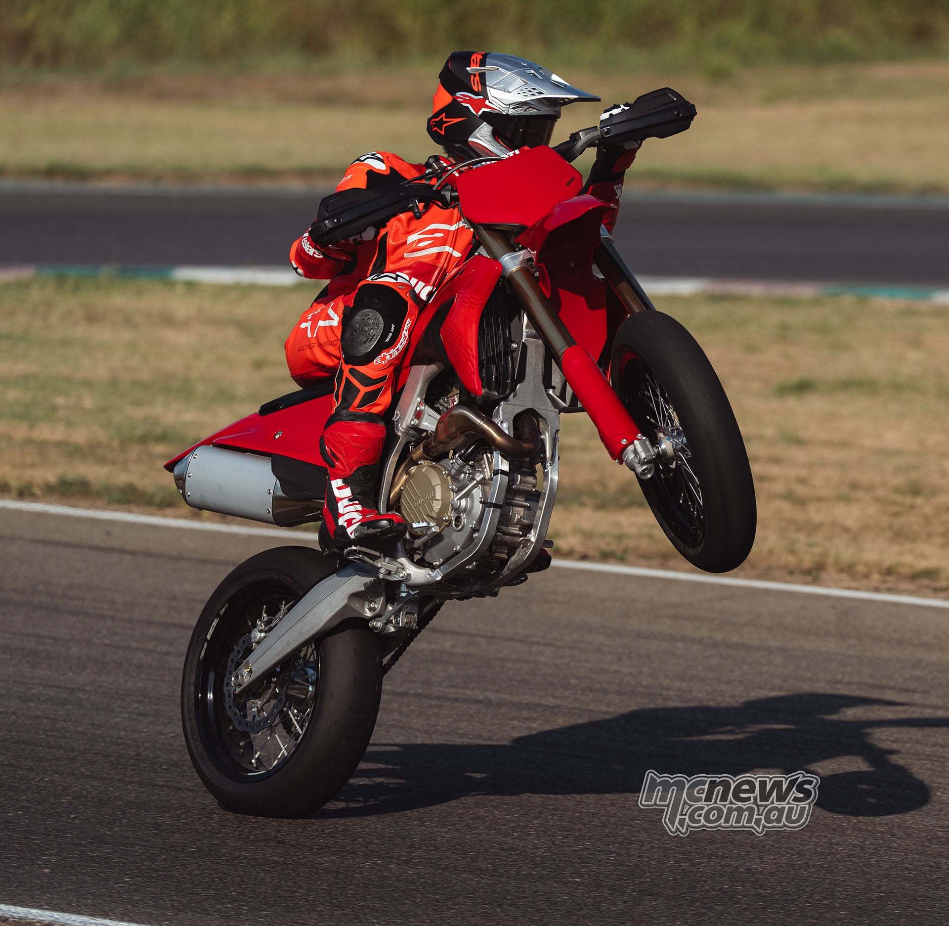 Ducati Desmo450 SM rider lifts the front wheel on a paved circuit, with the engine and exhaust visible beneath the red bodywork.