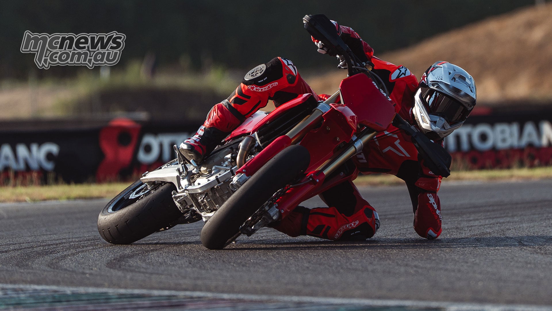 Ducati Desmo450 SM leaned deeply into a tarmac corner, with the rider's knee and elbow close to the track surface.